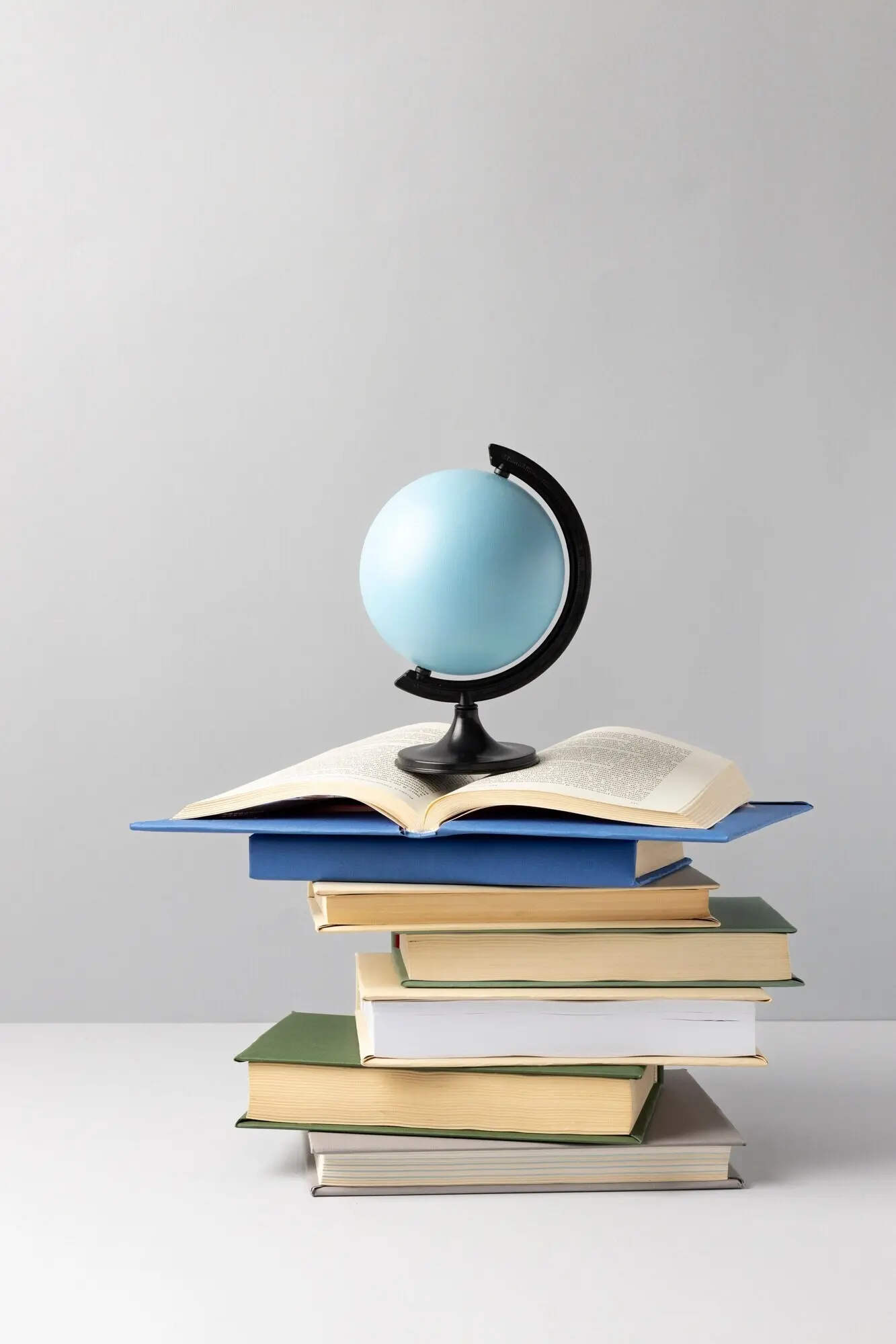 Ansicht von vorn mit gestapelten Büchern, einem Erdglobus und einem aufgeschlagenen Buch zum Tag der Bildung.